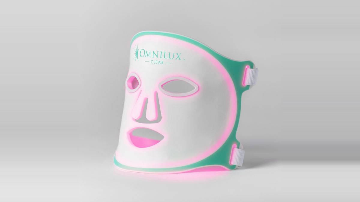 White and green Omnilux Clear LED mask, lit pink, on a grey background.