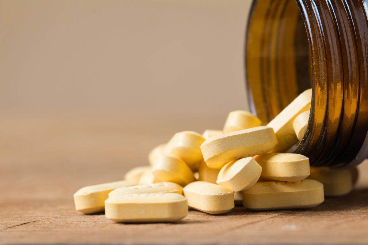 Yellow supplement tablets spilling from an amber glass bottle onto a wooden table.