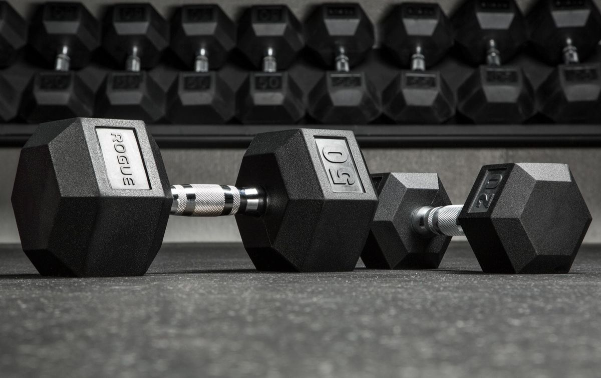 Rogue hex dumbbells on a gym floor with a rack of weights behind them