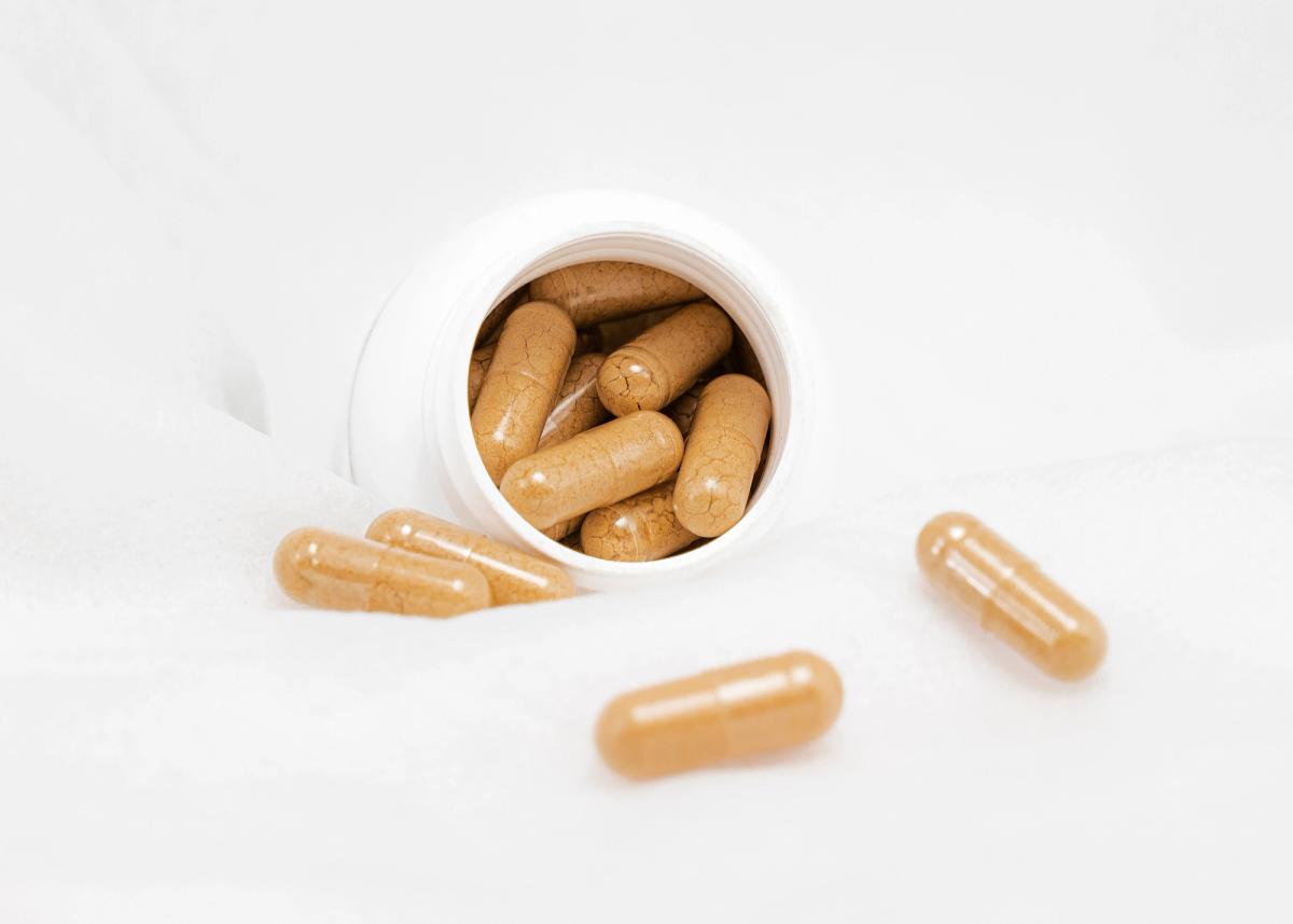 Tan supplement capsules spilling out of an open white bottle onto a white cloth surface