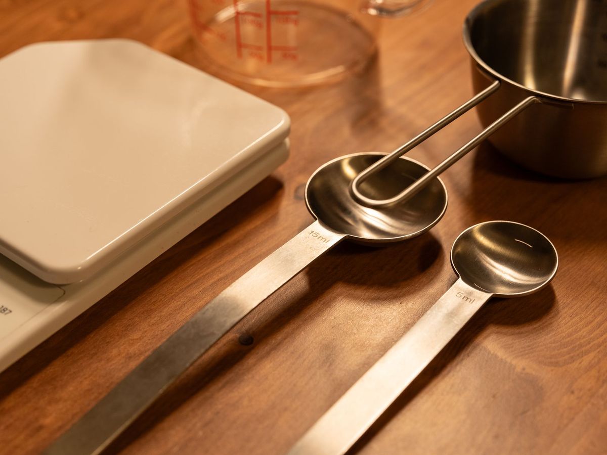 Unbranded kitchen scale beside measuring spoons and a measuring cup on a wooden counter