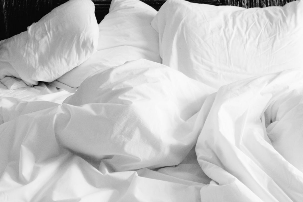 White sheets and a rumpled duvet on a bed.