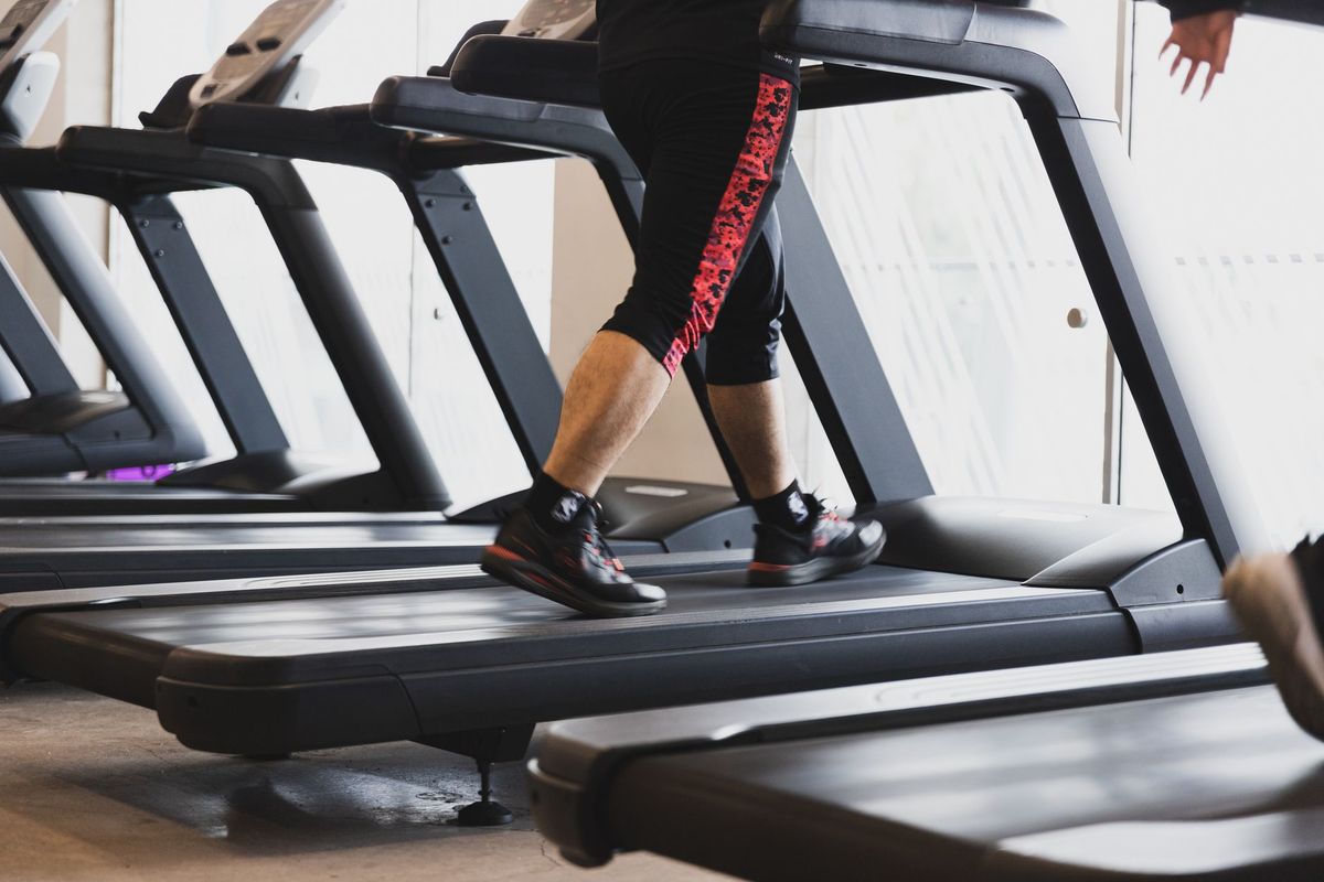 Person walking on a treadmill beside bright gym windows