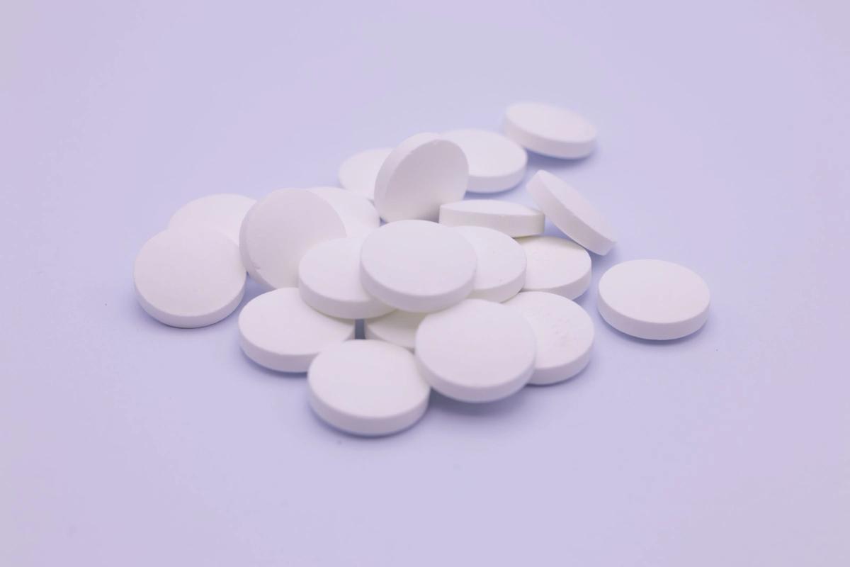 A small pile of round white tablets on a pale lavender background.