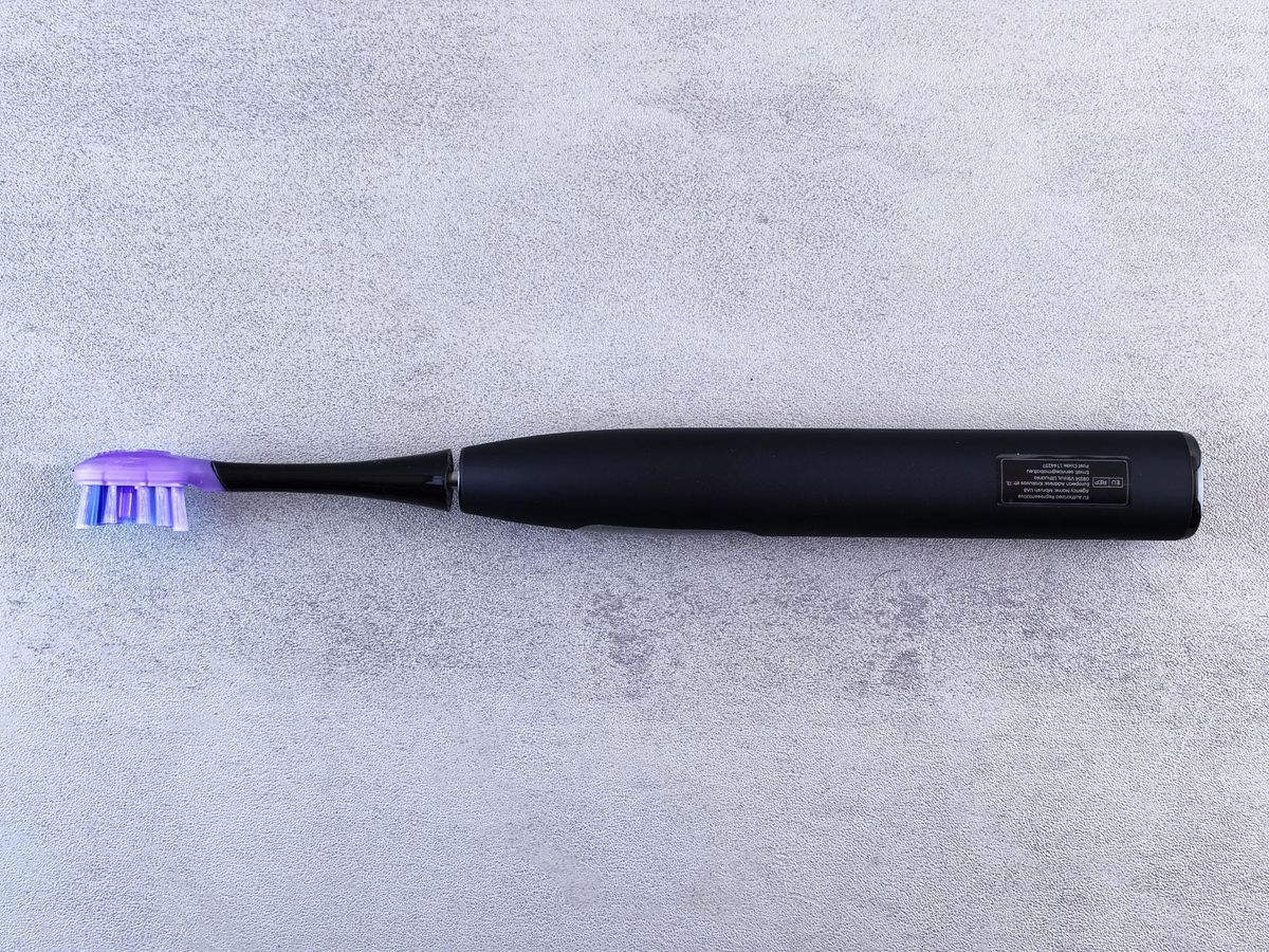 Black electric toothbrush with a purple head lying on a light gray surface.