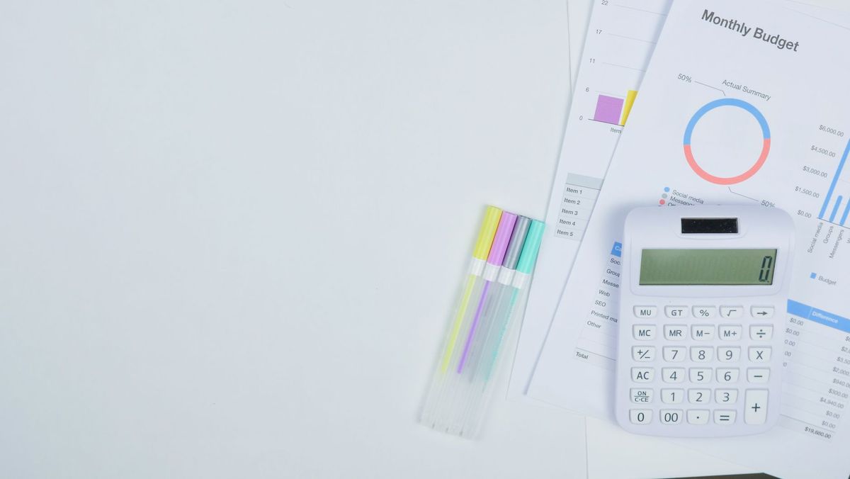 A white calculator and pastel pens beside monthly budget worksheets on a white desk.