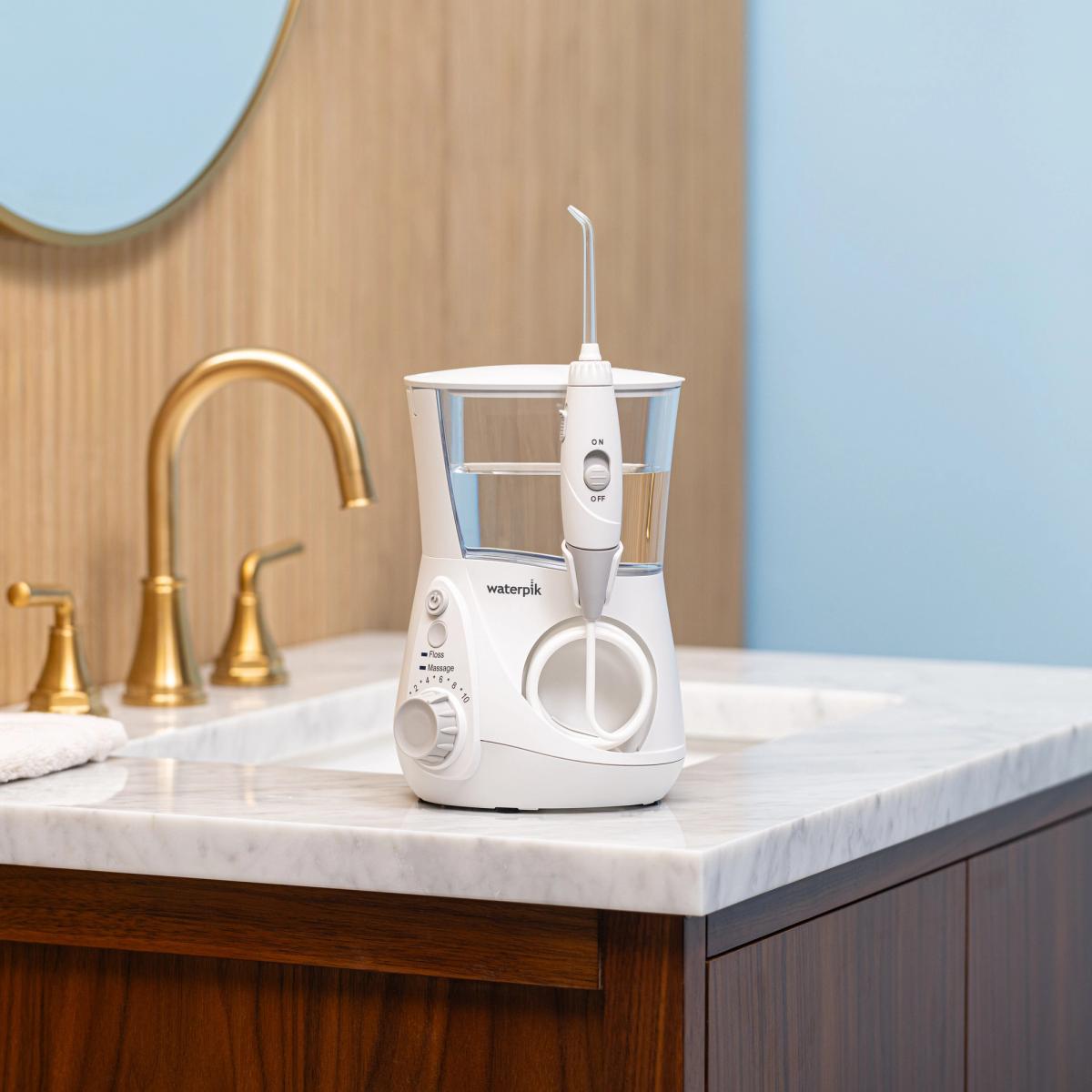 White Waterpik Aquarius water flosser on a marble bathroom counter beside a gold faucet.
