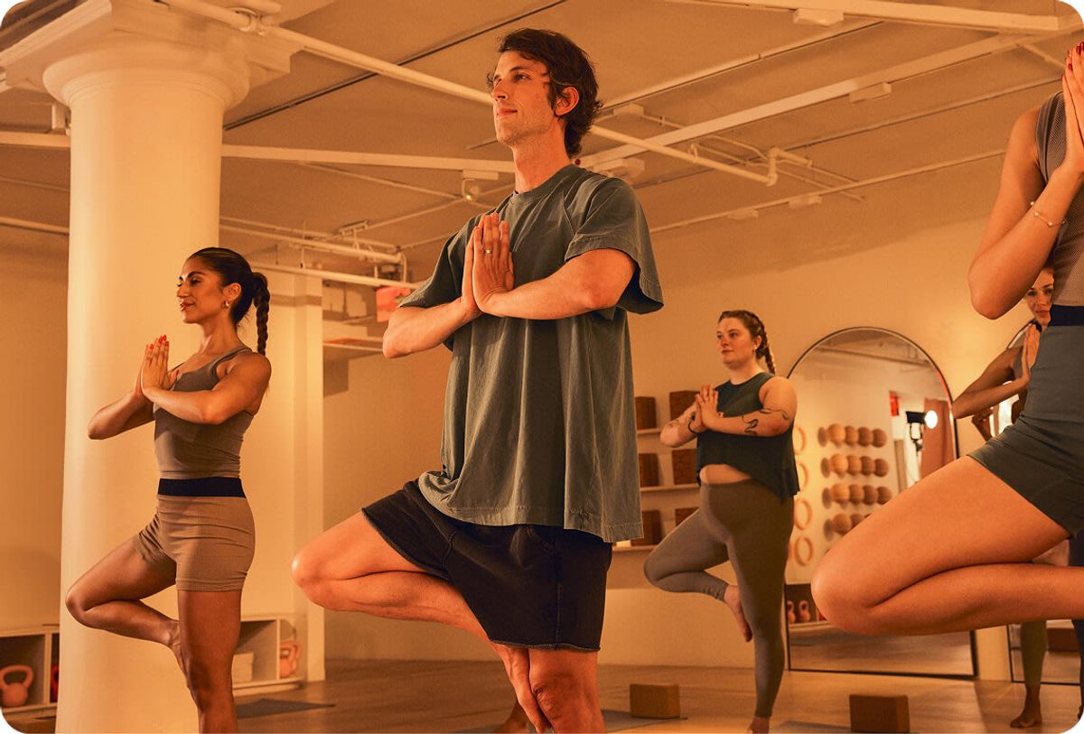 A group yoga class in a studio, several people balancing in tree pose.