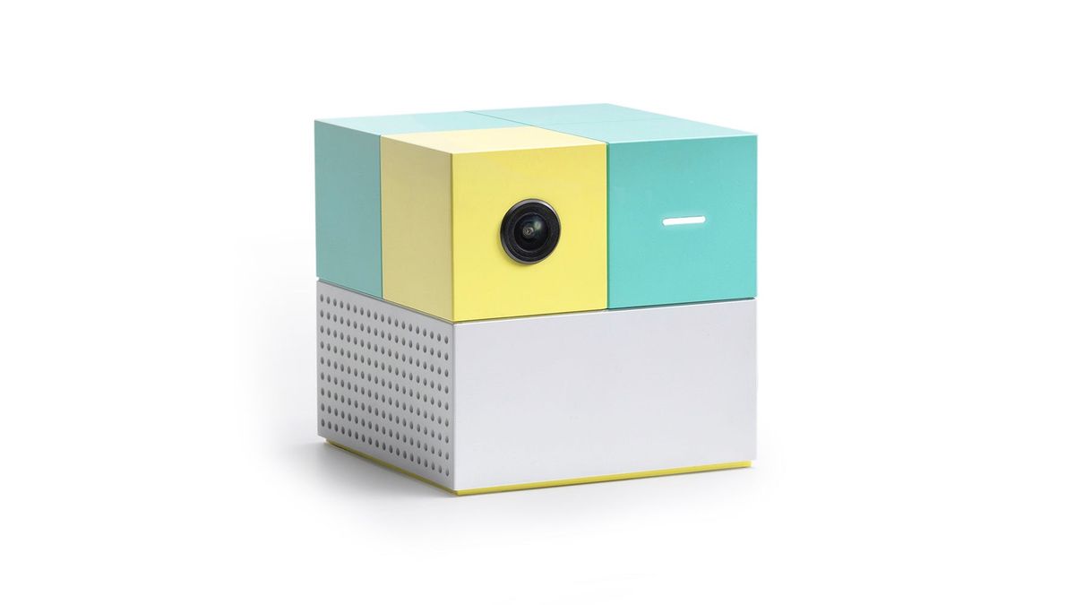 Nex Playground console, a small cube with a camera lens on its yellow and turquoise top and a white base, on a white background.