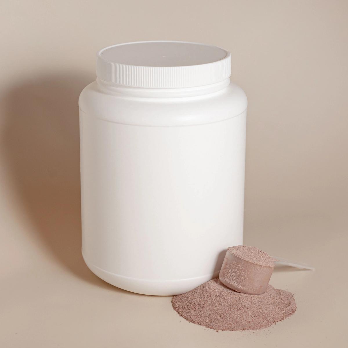 A scoop of protein powder resting beside an unlabeled white container on a clean, bright surface.