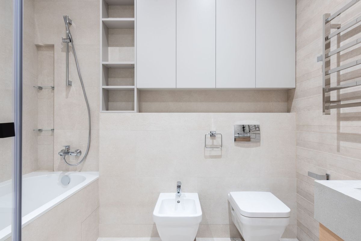 White bidet beside a toilet in a light tiled bathroom.