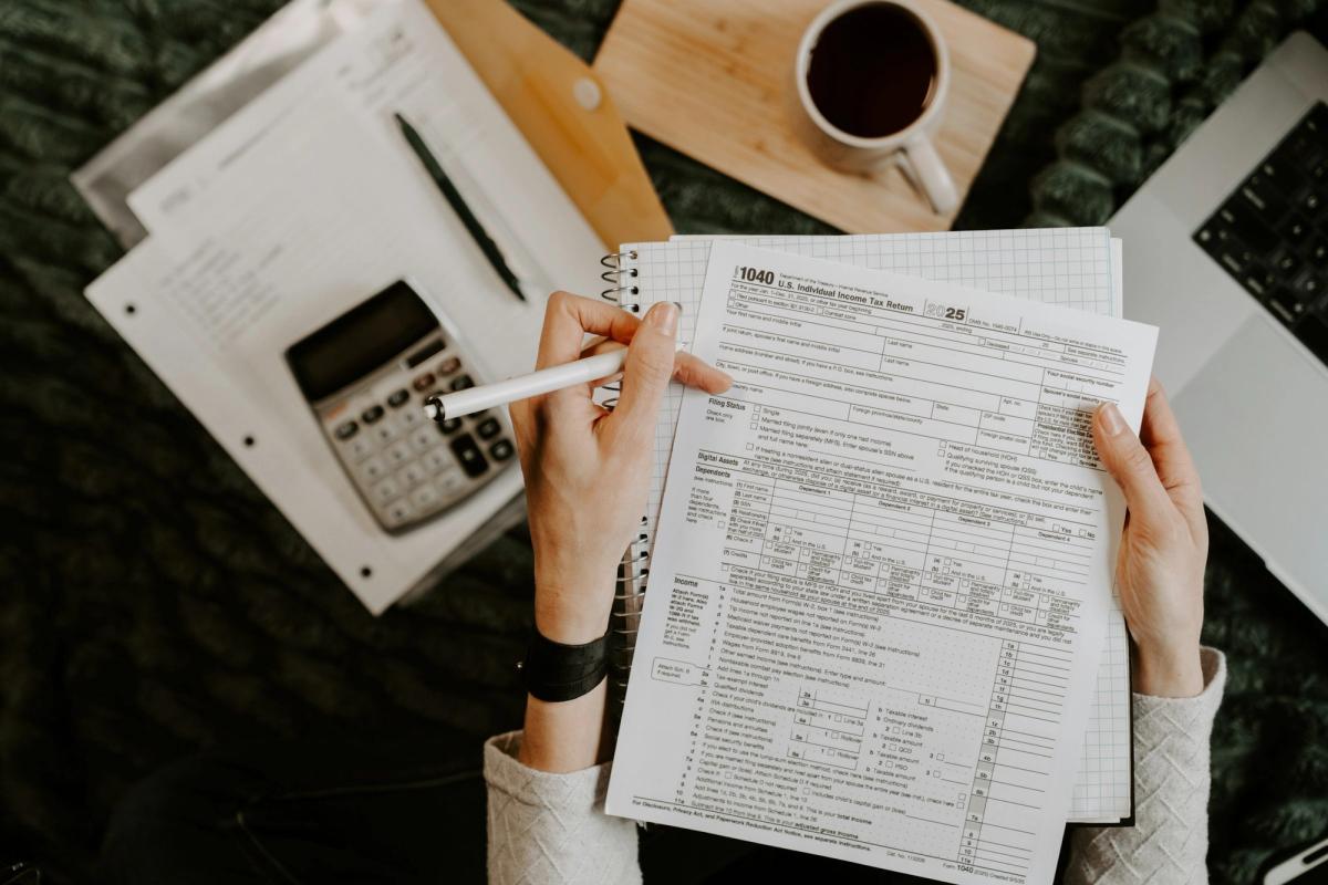 Person reviewing a federal tax form with a calculator, laptop, and coffee at a desk