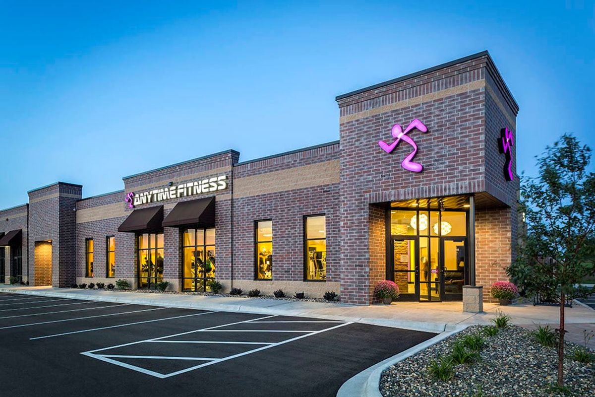 Brightly lit Anytime Fitness gym exterior at dusk in a modern brick building with parking lot; part of Crates Health's fitness and wellness services.