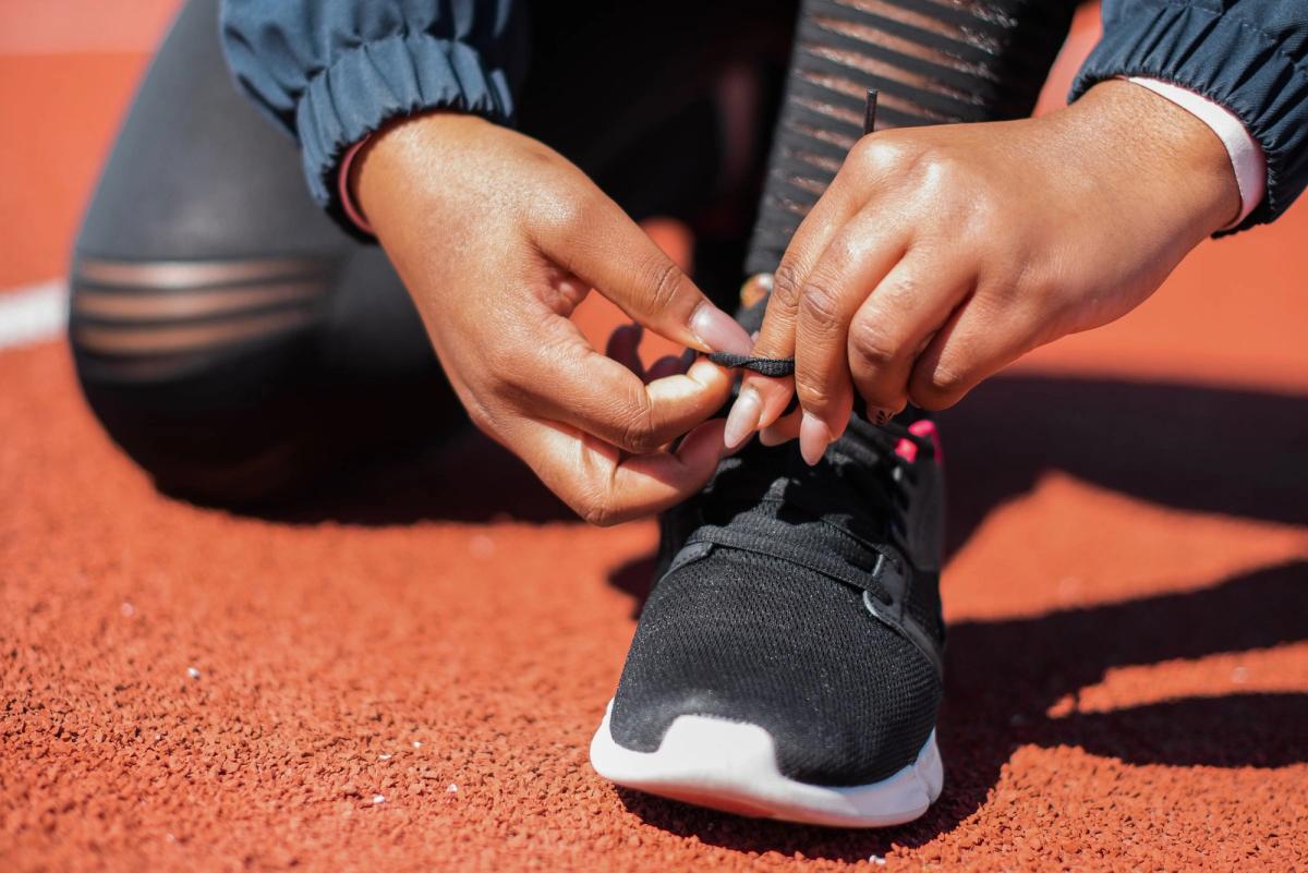 A runner ties the laces of a black athletic shoe on a running track