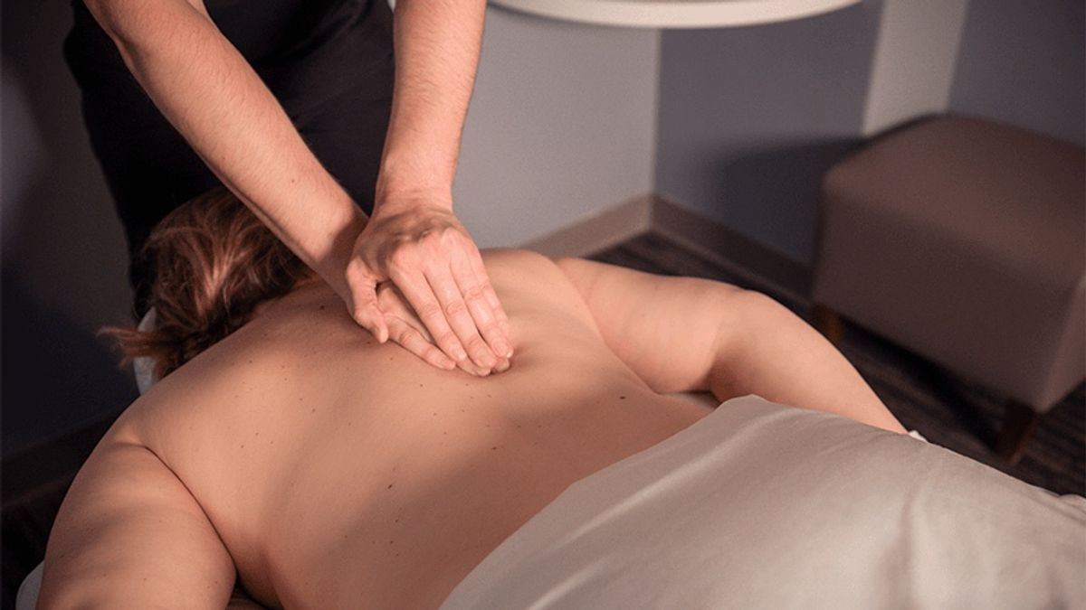 A massage therapist works on a client's upper back in a Massage Envy treatment room.