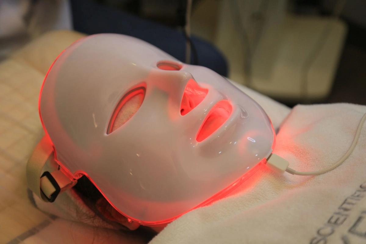 Person wearing a white LED face mask glowing red while reclining.