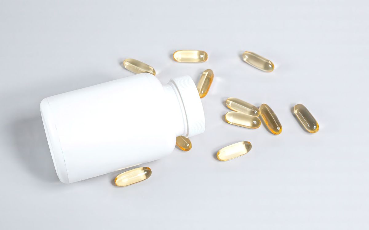 Golden fish oil softgels beside an open white supplement bottle