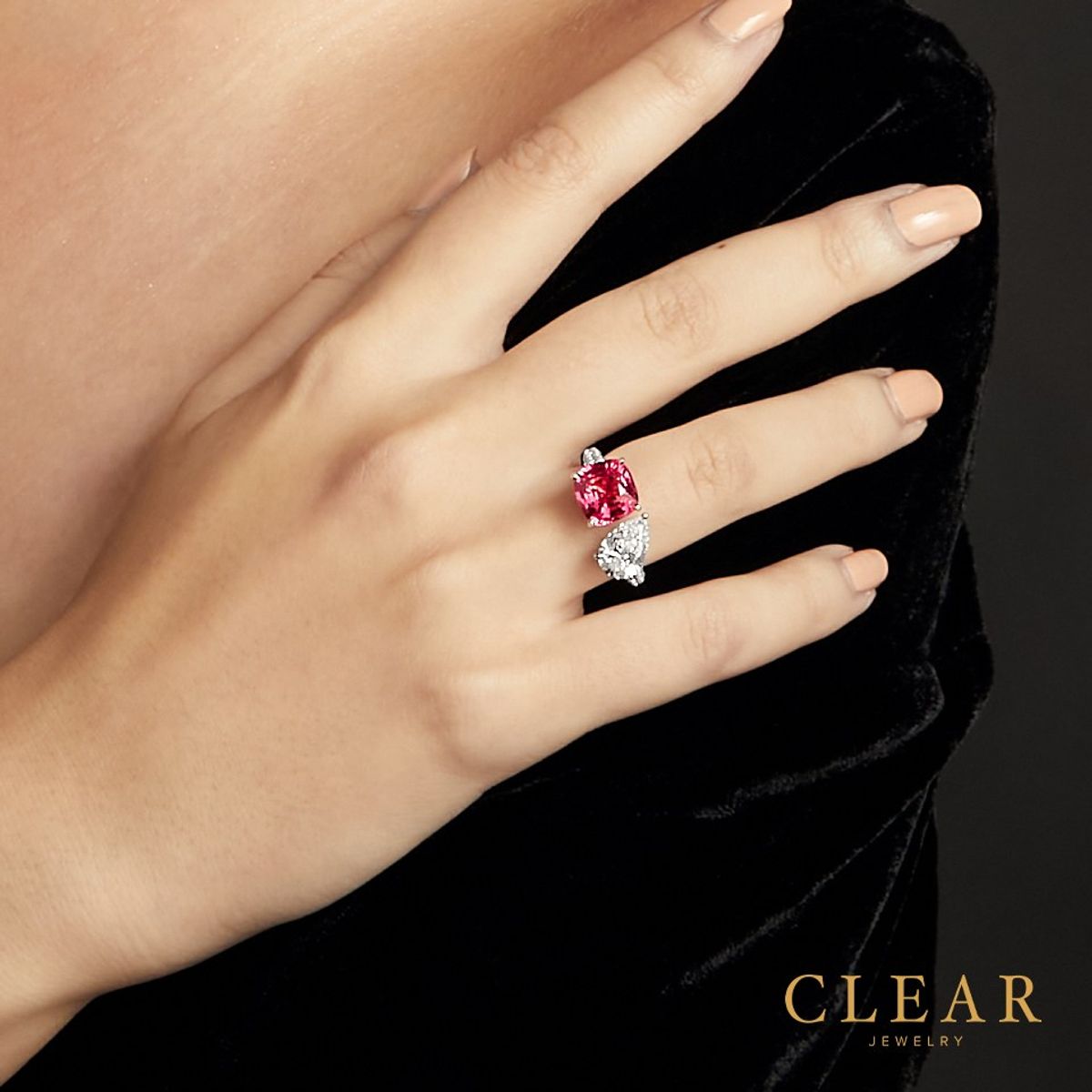 Cushion pink spinel and pear diamond bypass ring on a hand against black velvet.