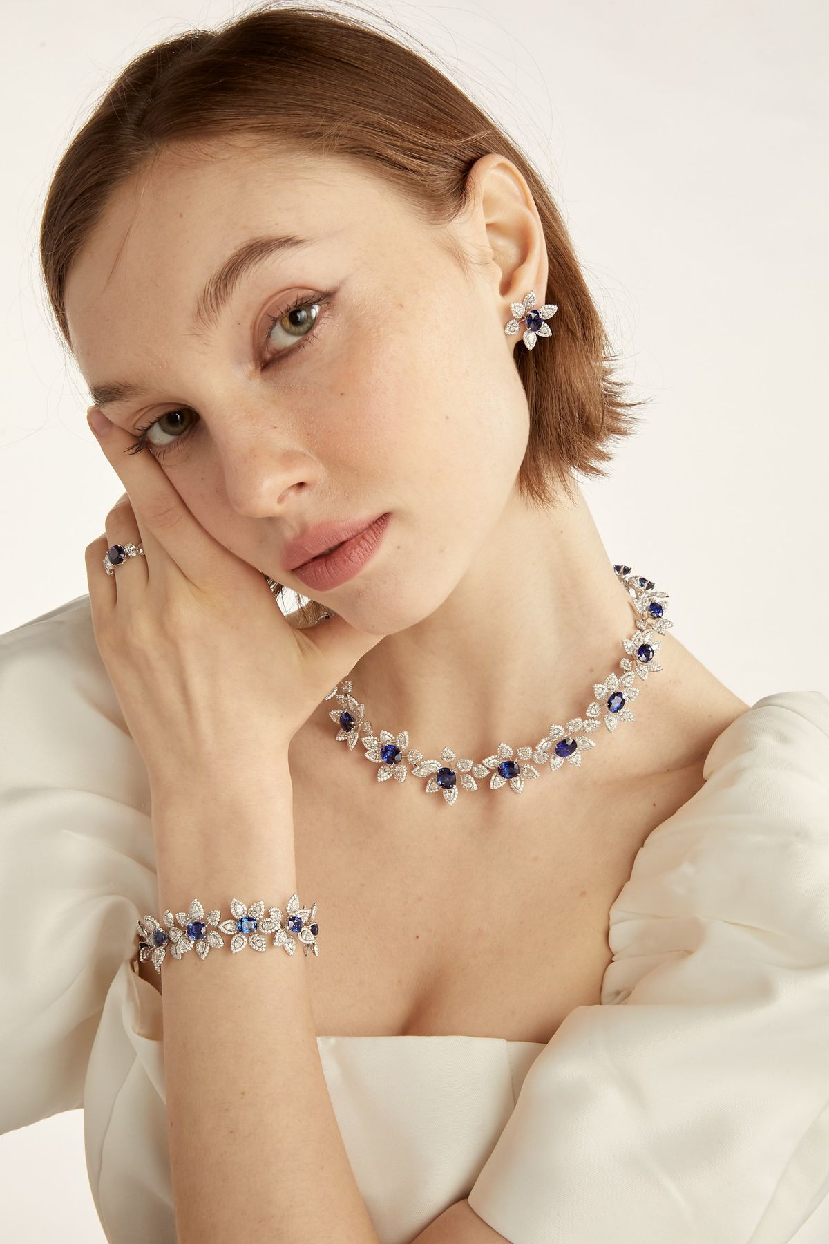 Close model portrait wearing the sapphire floral necklace, earring and ring.