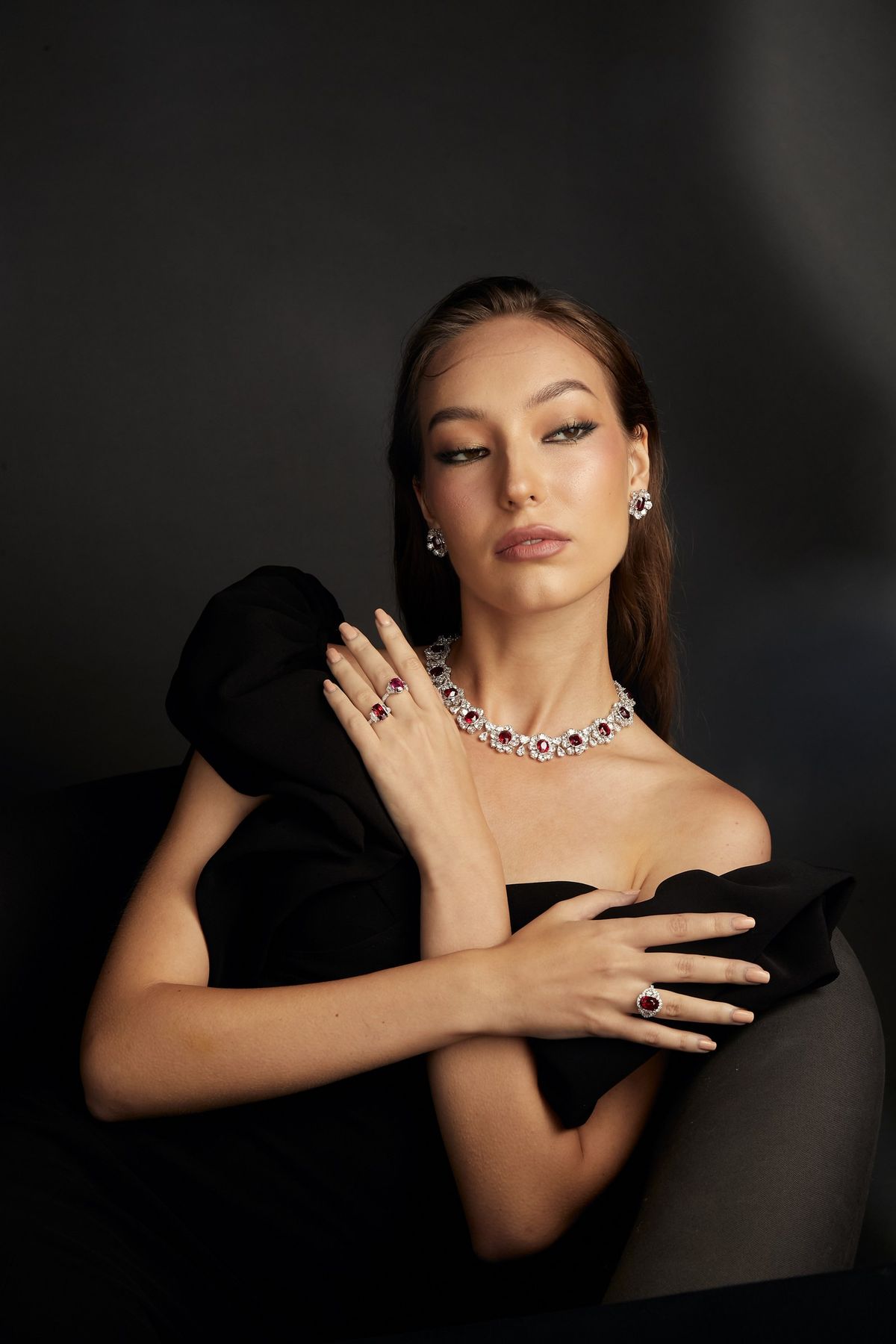 Model in black holding a Burmese ruby parure — necklace, ring and earrings.