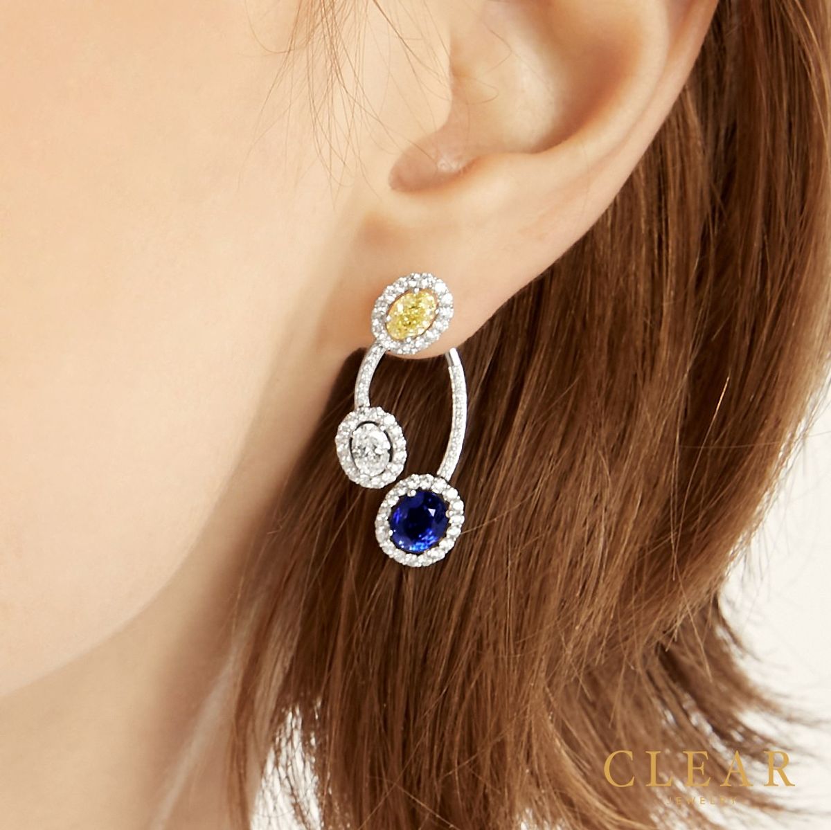 Single-ear shot of an orbit drop earring with a yellow sapphire and a royal blue sapphire.