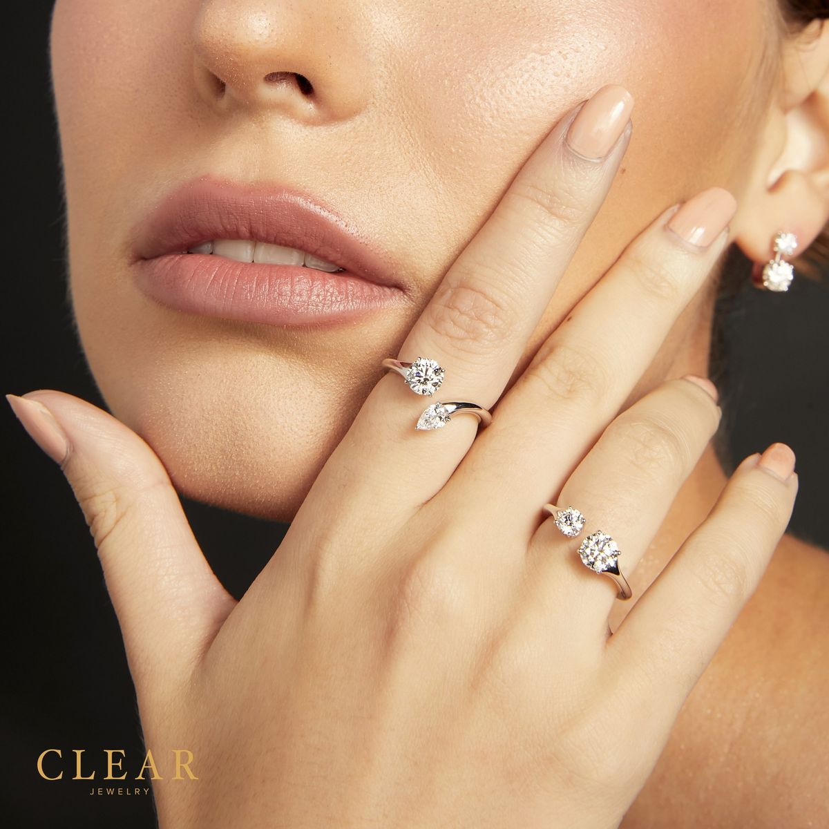 Model hand at face wearing a solitaire and a pear-bypass diamond ring.