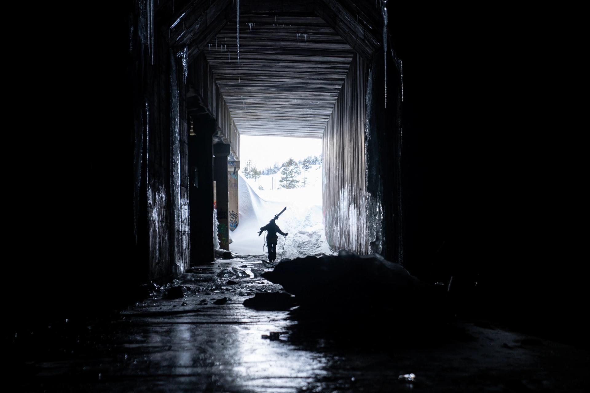 Snowboarder walking out of the dark Donner Summit railroad snowshed toward daylight