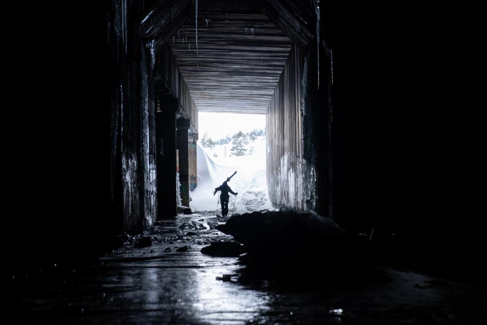Snowboarder walking out of the dark Donner Summit railroad snowshed toward daylight