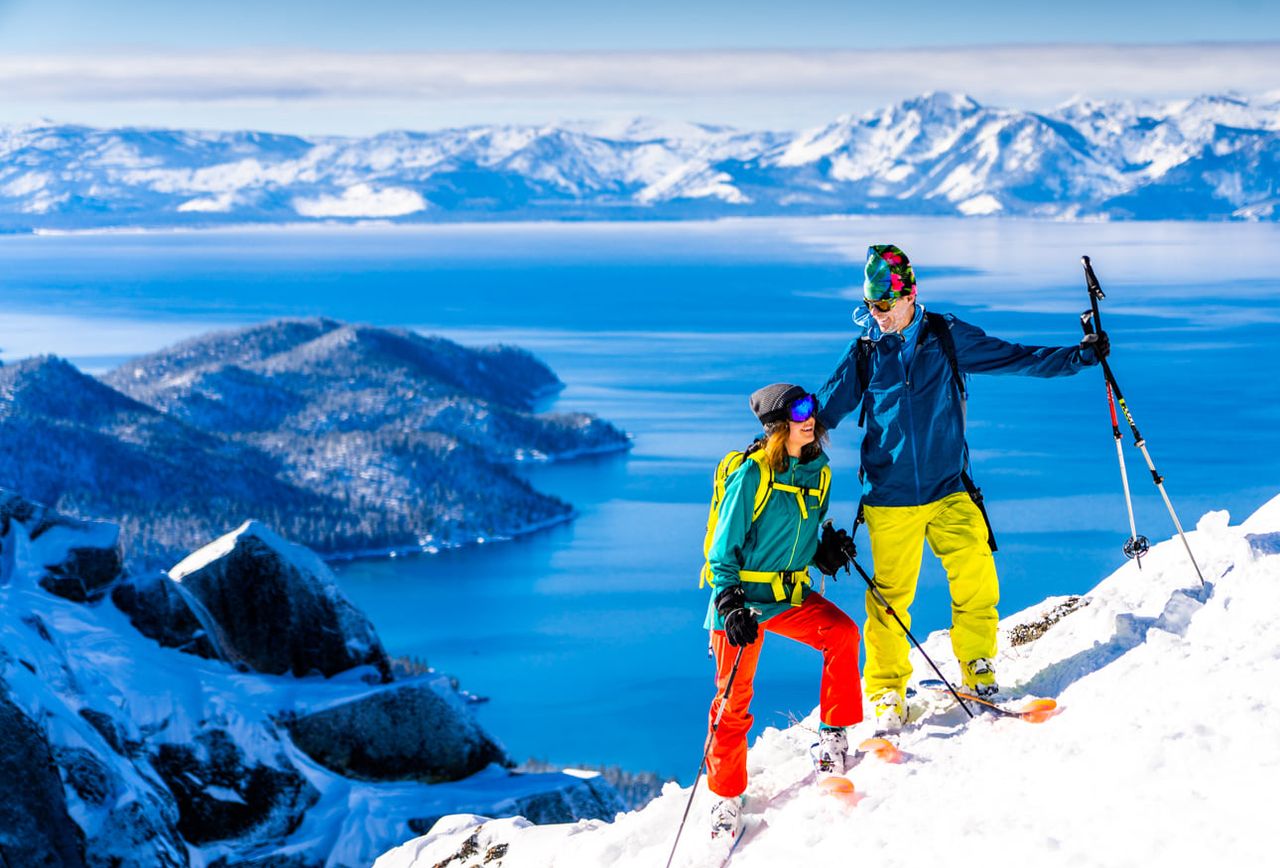Two backcountry skiers on a snowy summit above Emerald Bay and Lake Tahoe