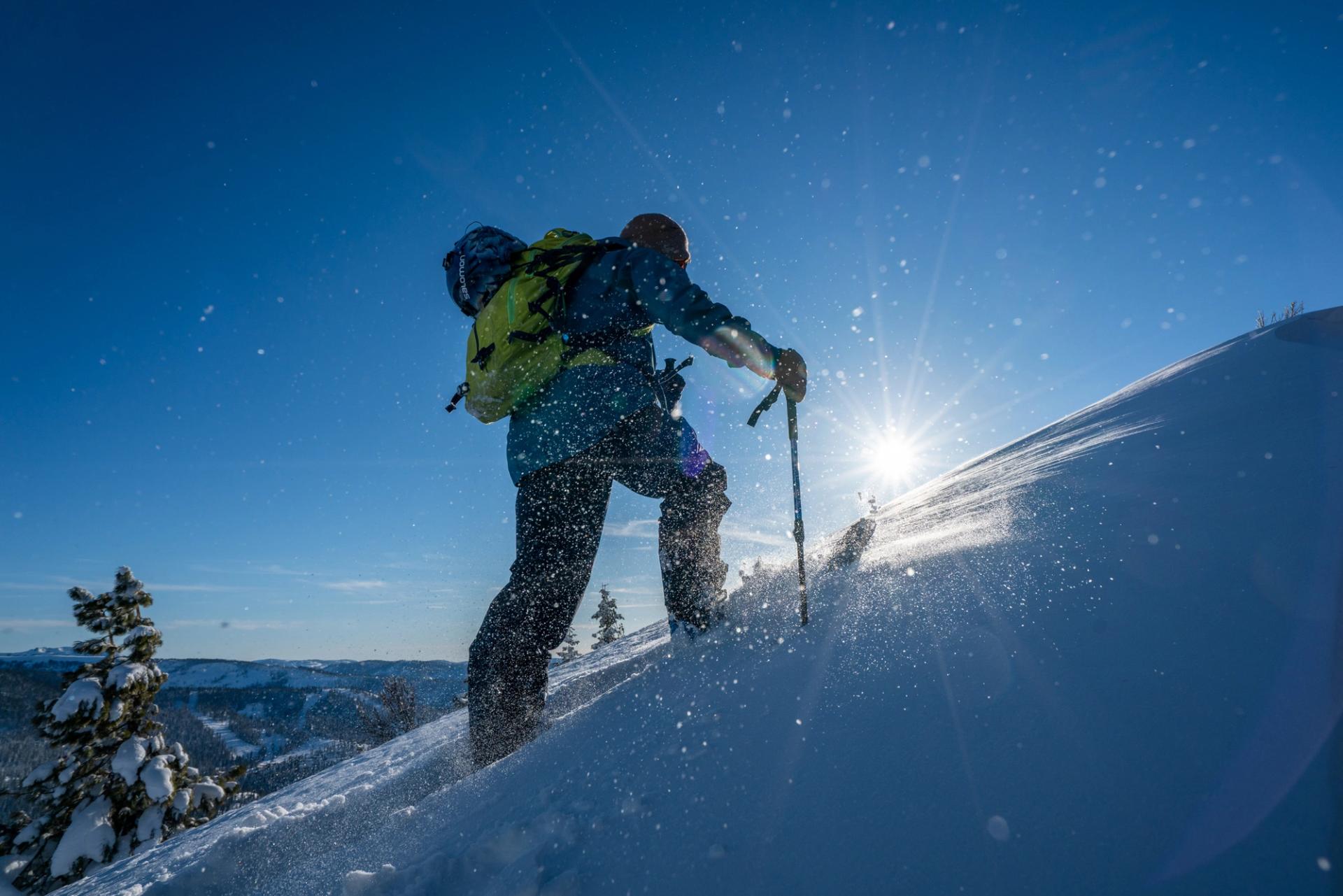 Splitboarder skinning up a sunlit slope with Lake Tahoe below