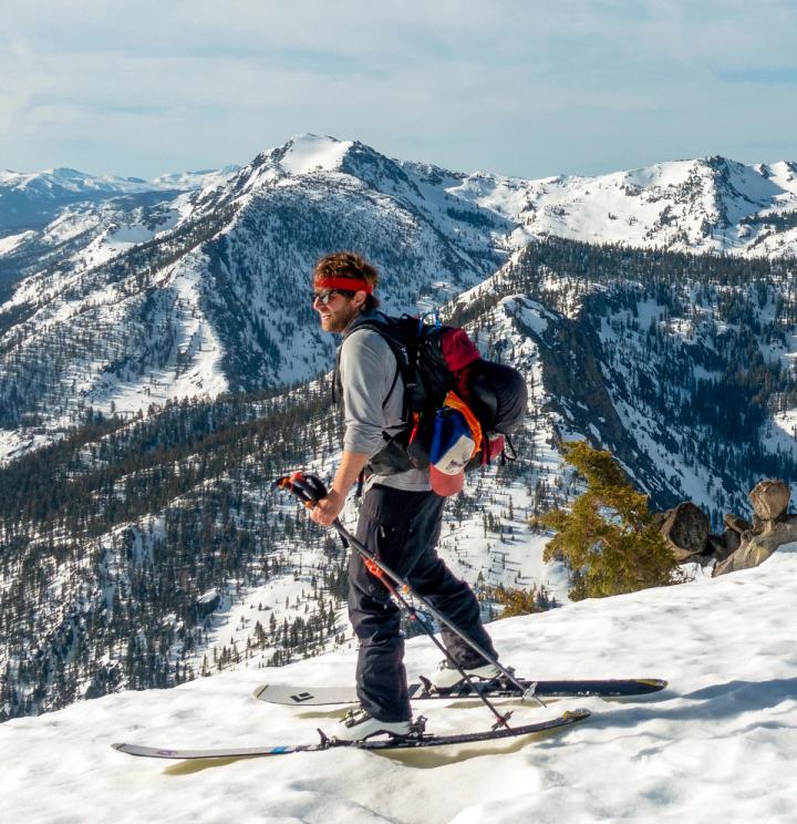 Steve Byrne ski touring on a snowy ridge with mountains behind