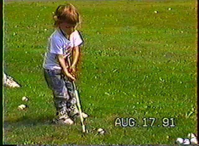 two year old addressing a golf ball on a grass driving range