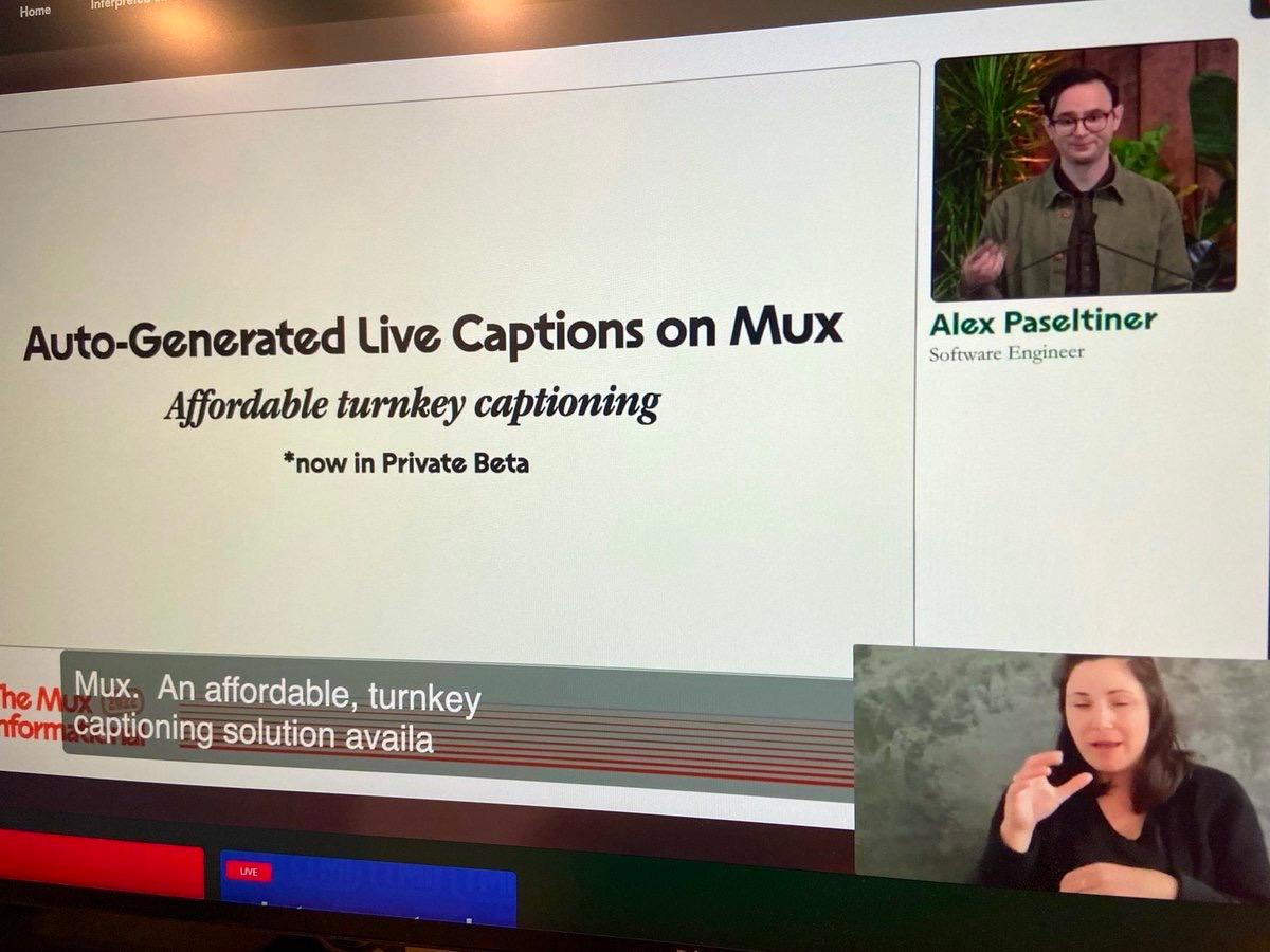 Close-up of a monitor depicting a man named Alex Paseltiner (Software Engineer) on stage alongside his presentation slides, which read, "Auto-Generated Live Captions on Mux. Affordable turnkey captioning. *now in Private Beta". An ASL interpreter is also visible on screen.
