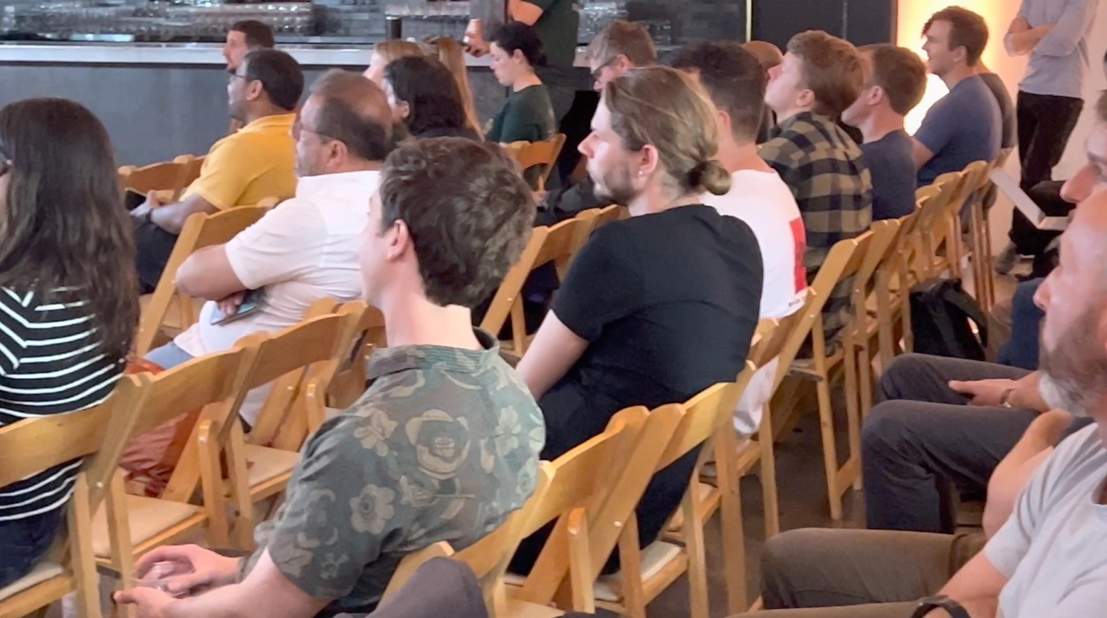 Four rows of wooden chairs with people sitting in them.