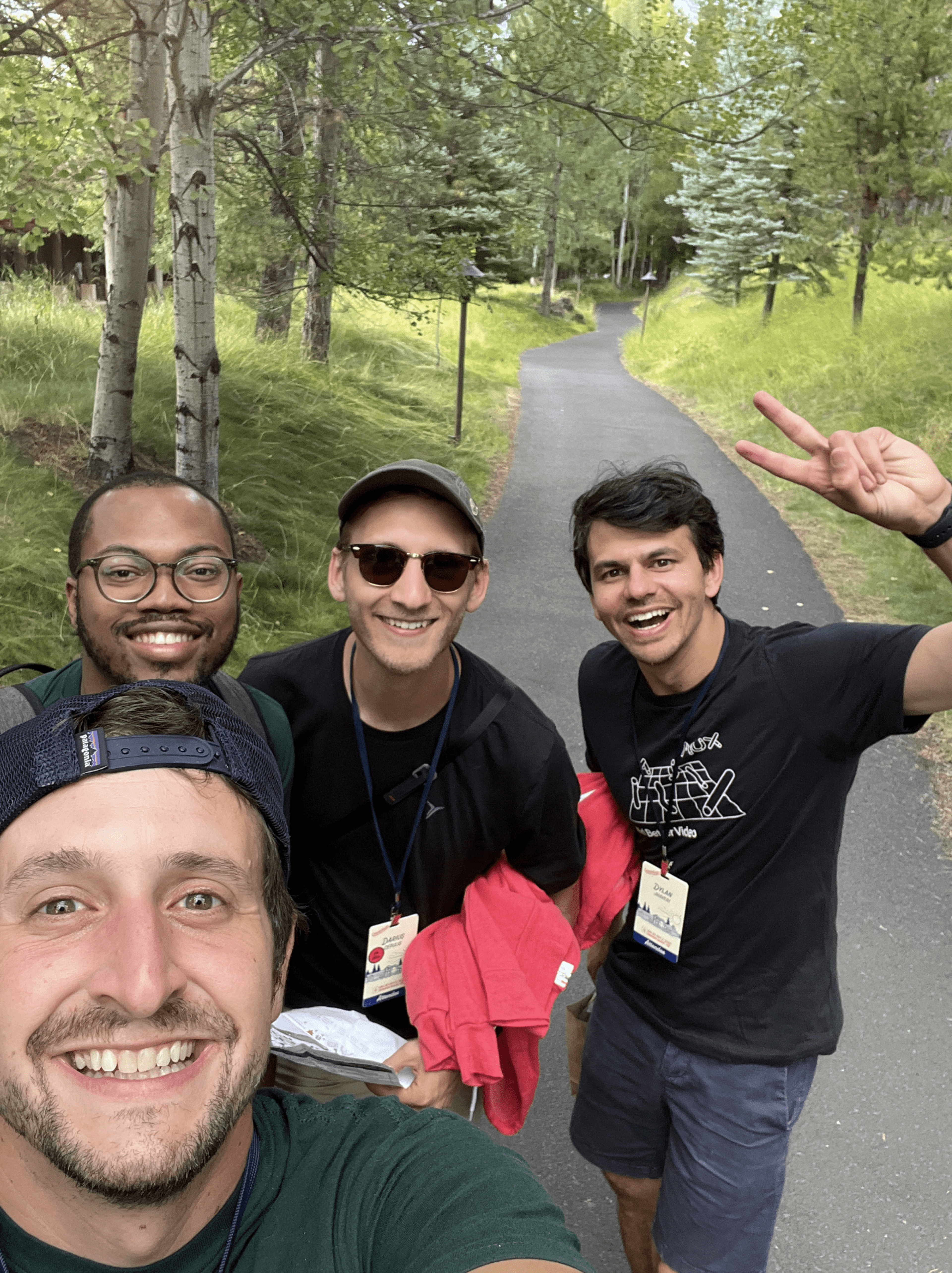 A group of four men smiling at the camera on a walking path outdoors