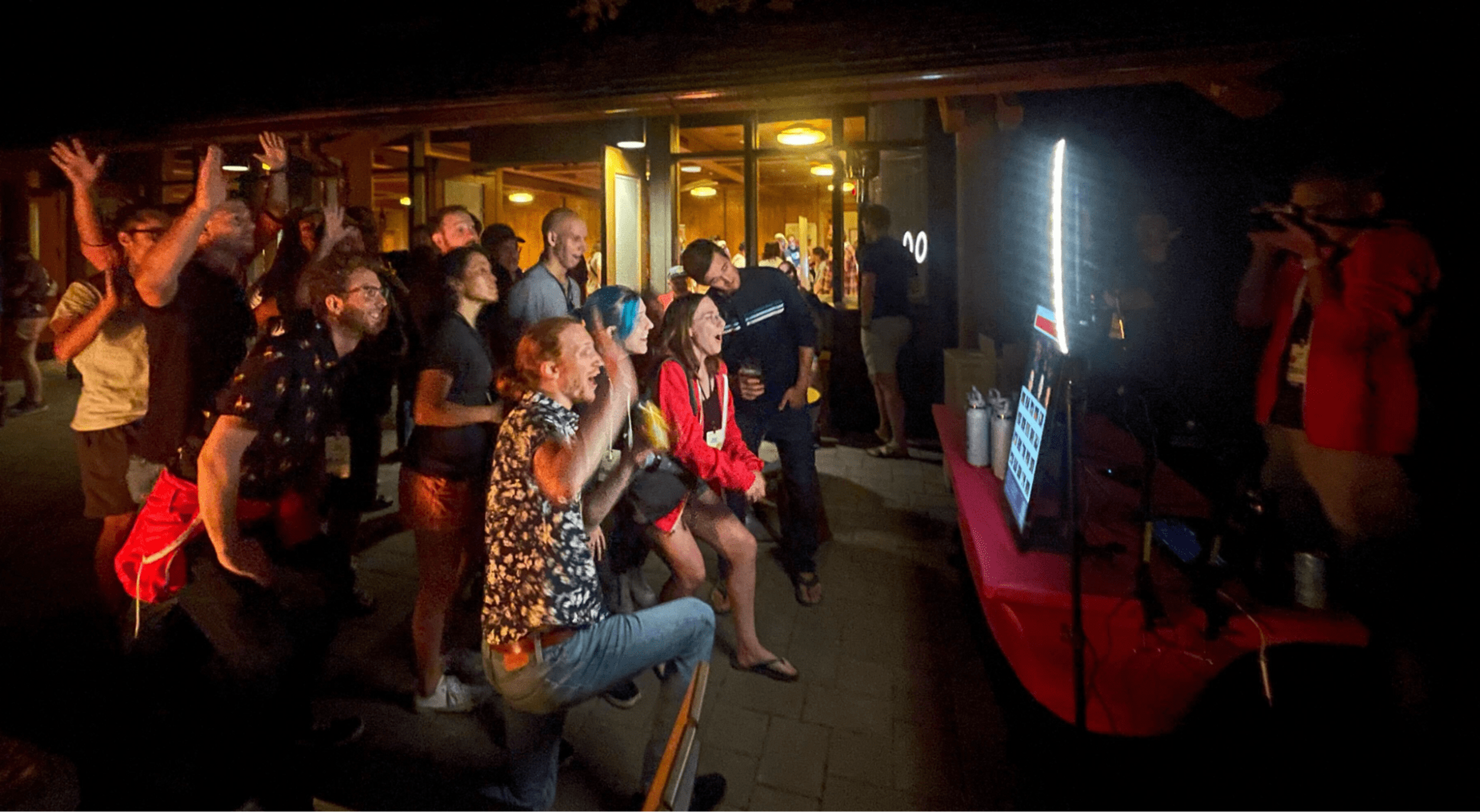 A group of people standing in front of the video guestbook outside at night time.