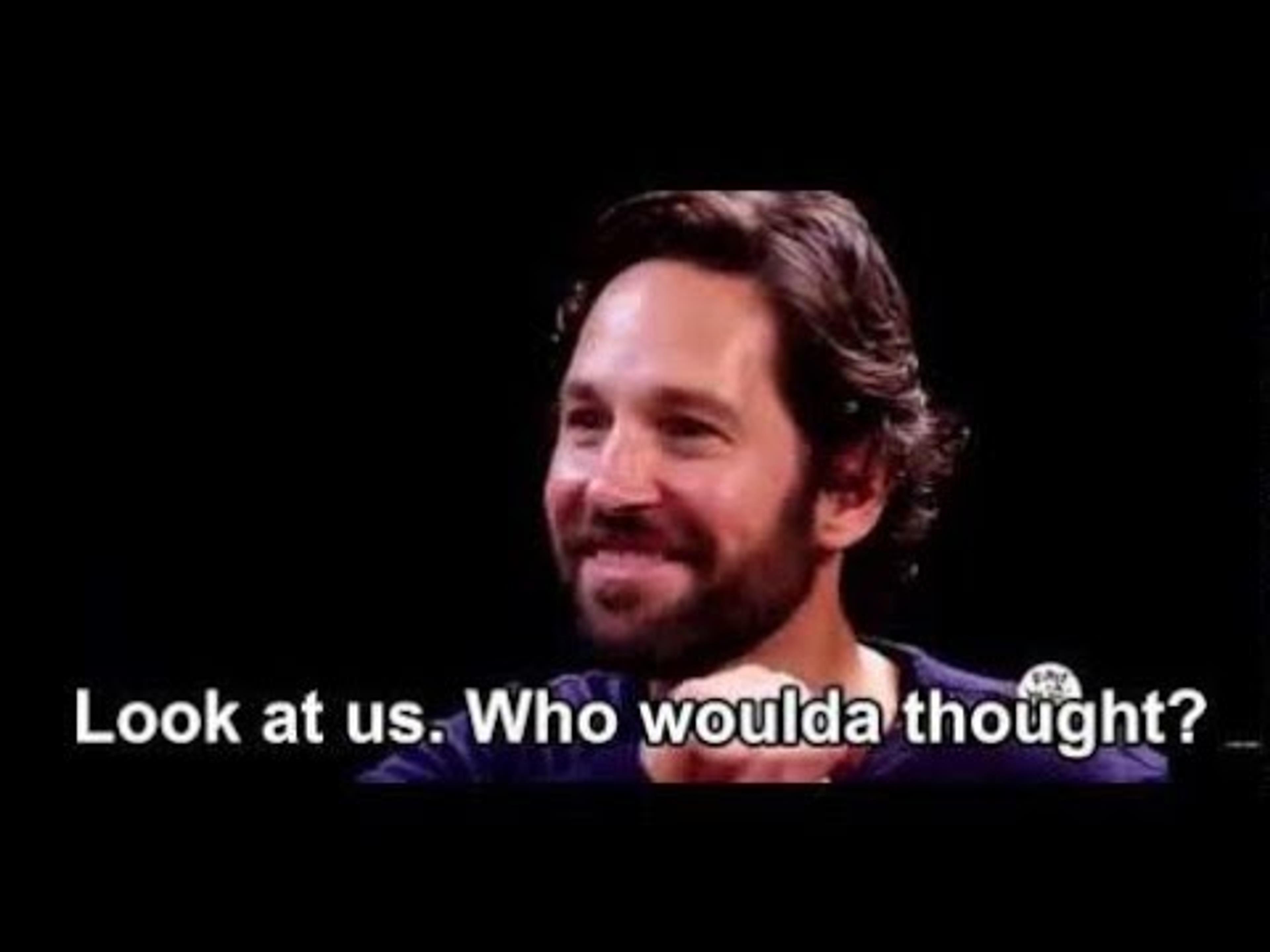 Paul Rudd sitting at a table and smiling saying, "Look at us. Who woulda thought?"