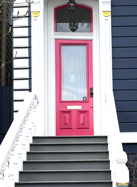 A medium close-up photo of a house entryway, the front door is painted pink.