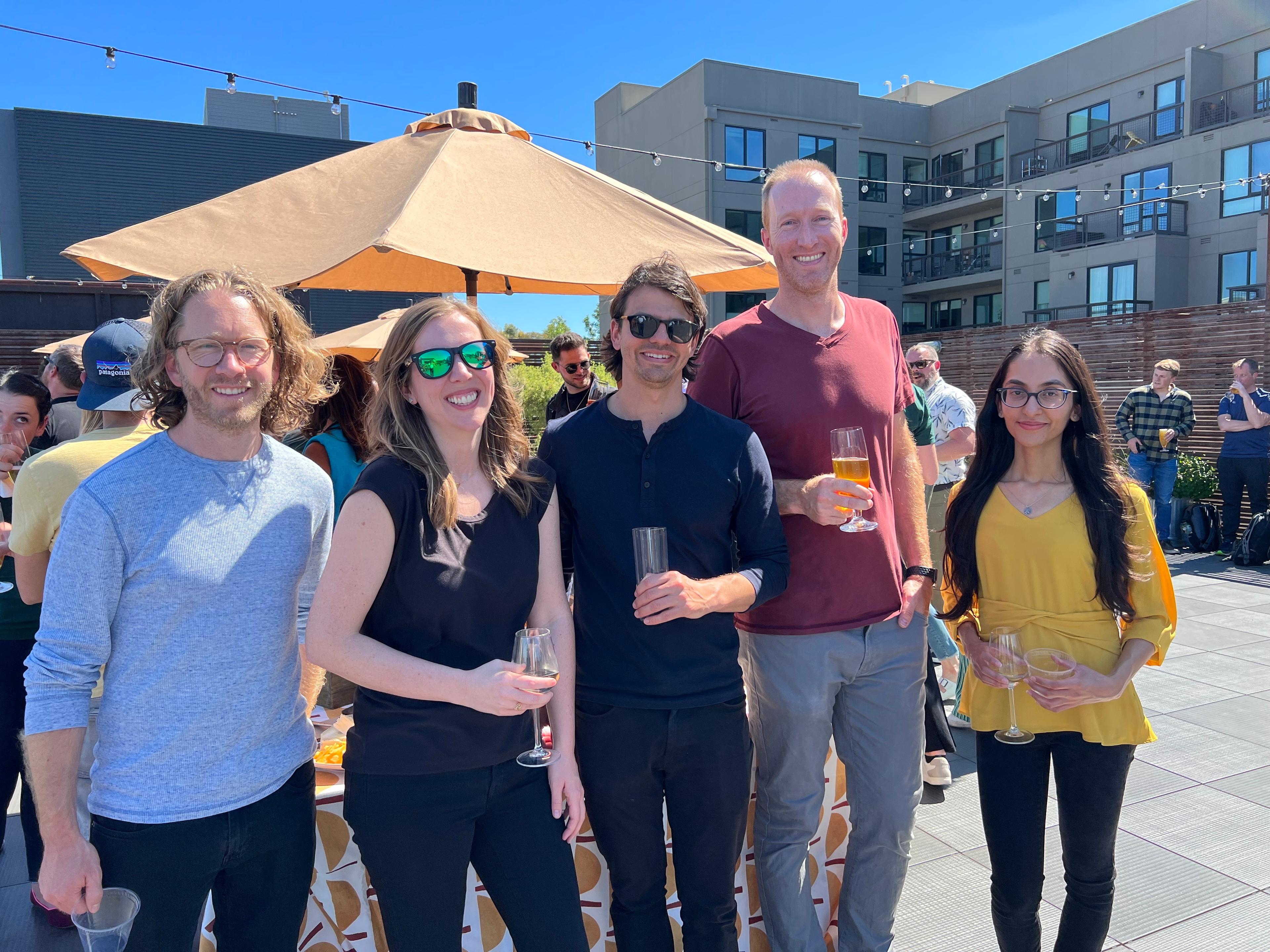 A group of people smiling holding drinks on a rooftop patio.