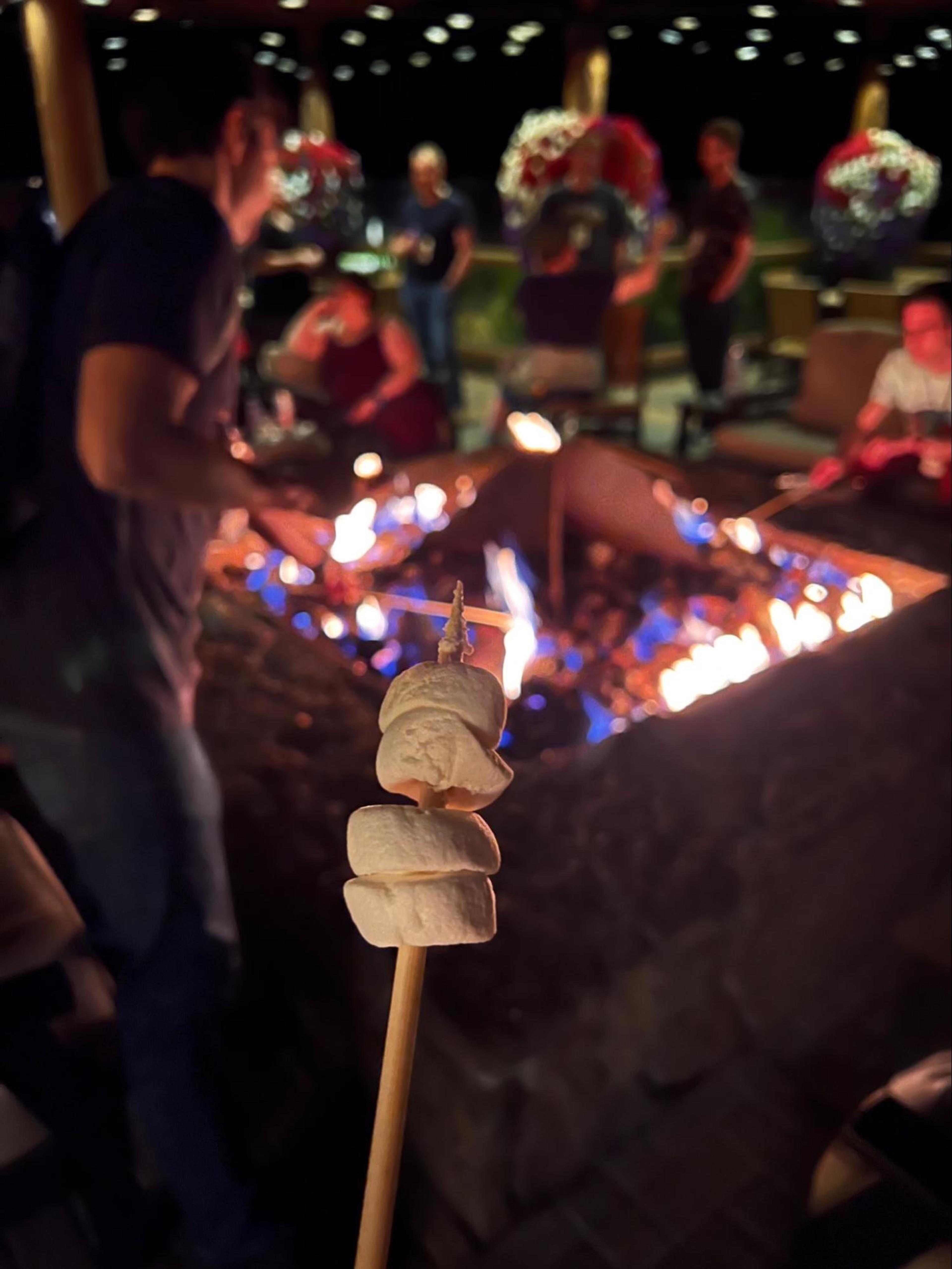 A stick holding several marshmallows being roasted over a campfire