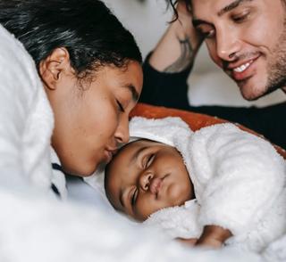 Parents laying in bed with baby looking happy