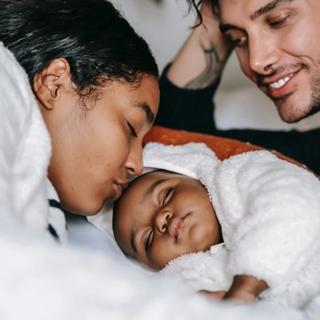 Parents laying in bed with baby looking happy