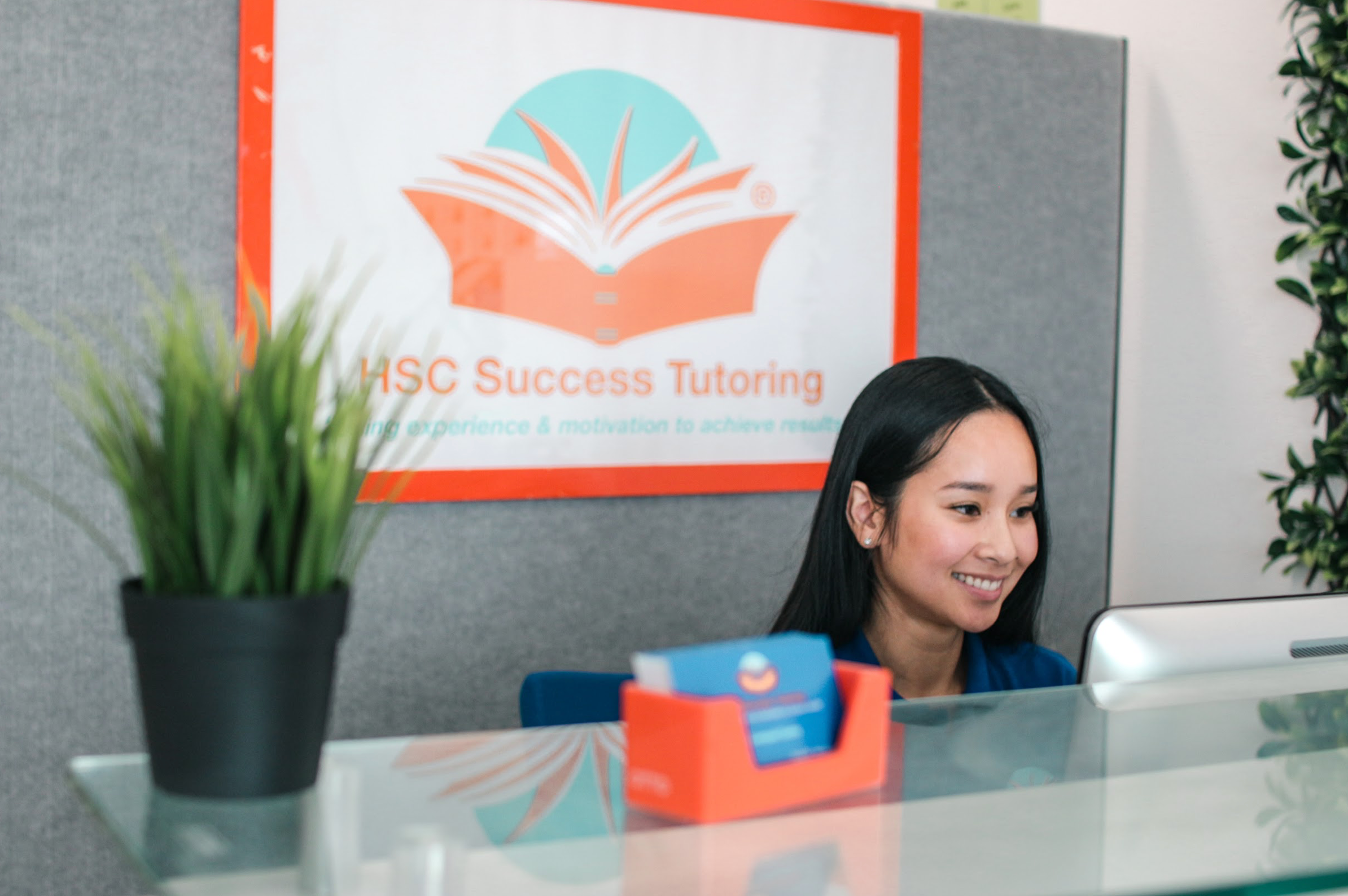 a woman sits at a desk in front of a sign for hsc success tutoring