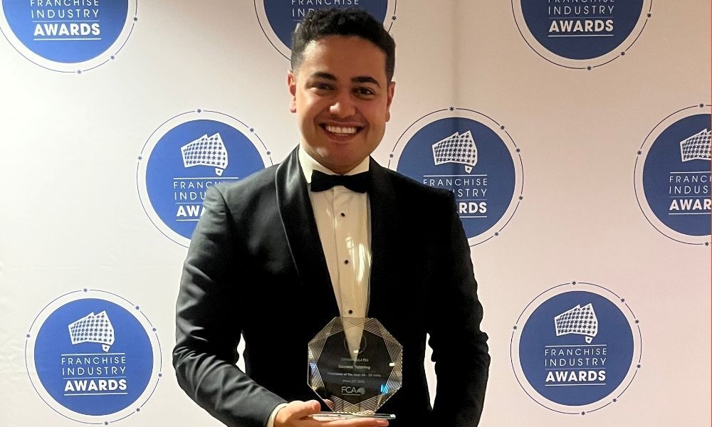 a man in a tuxedo is holding a trophy in front of a wall of awards .