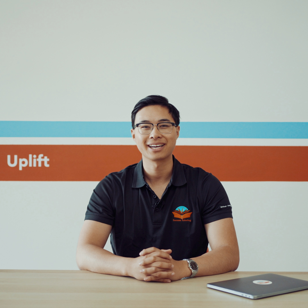 a man sits at a desk in front of a wall that says uplift