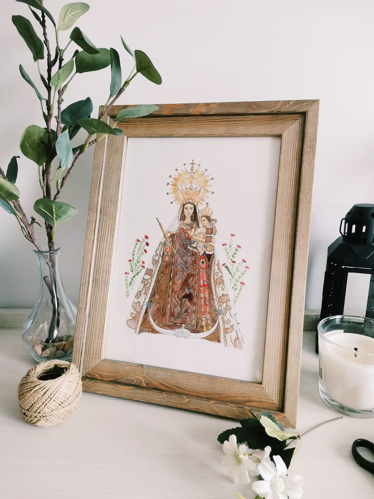 Ilustración de la Virgen en acuarela, enmarcada sobre una mesa