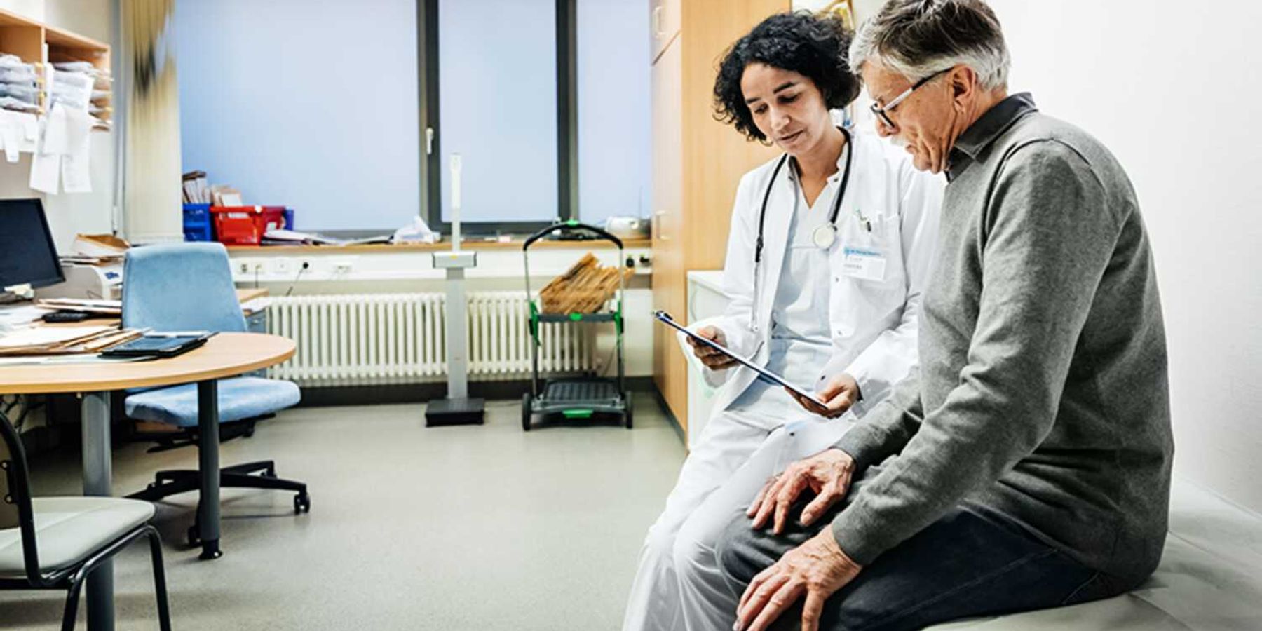Doctor showing a tablet to an older patient during a clinic consultation