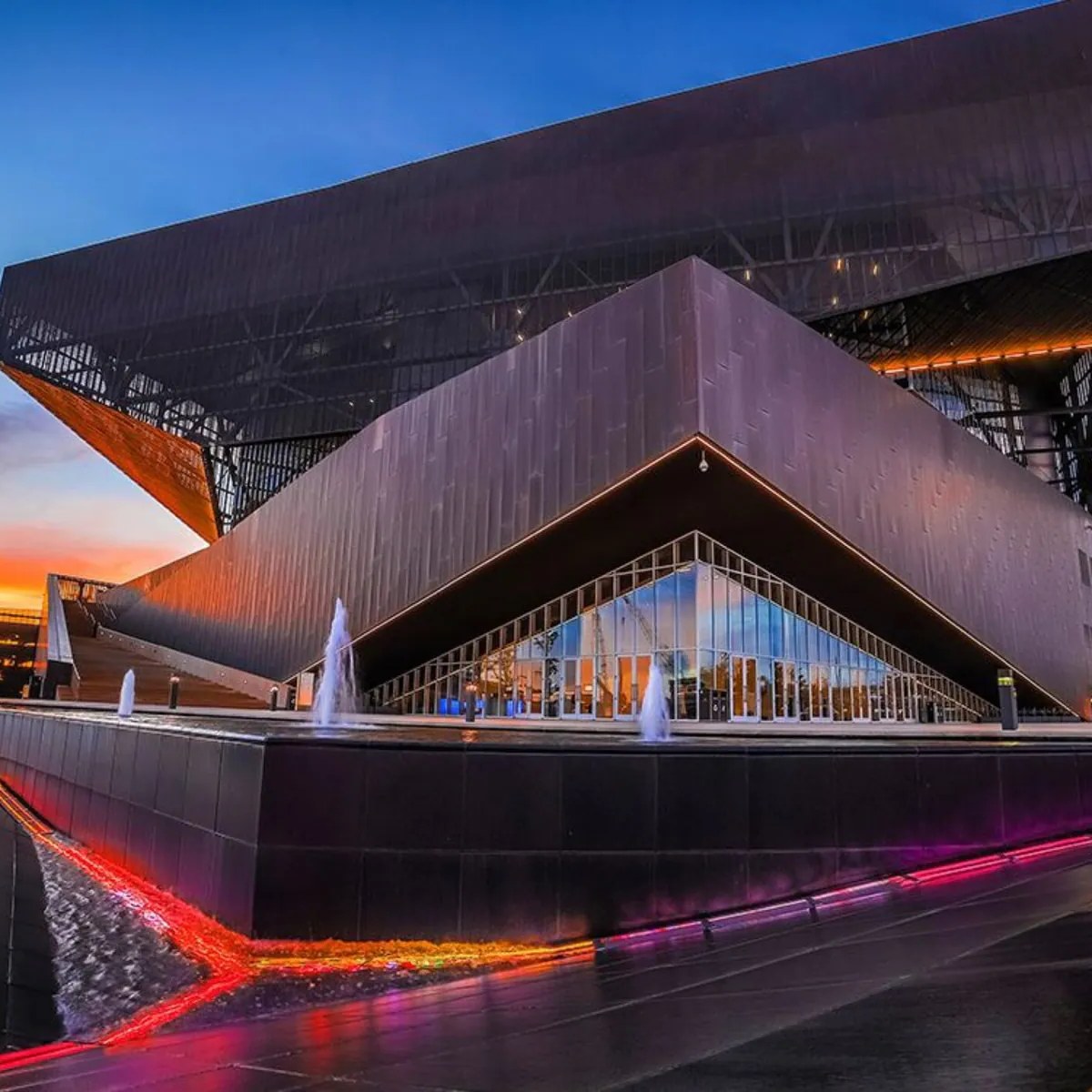 An angular convention venue at dusk with pink light trails