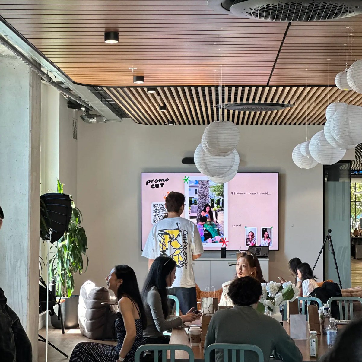 Guests gathered at the PromoCut x Cafe Jœ creator event while a presenter stands in front of a PromoCut display
