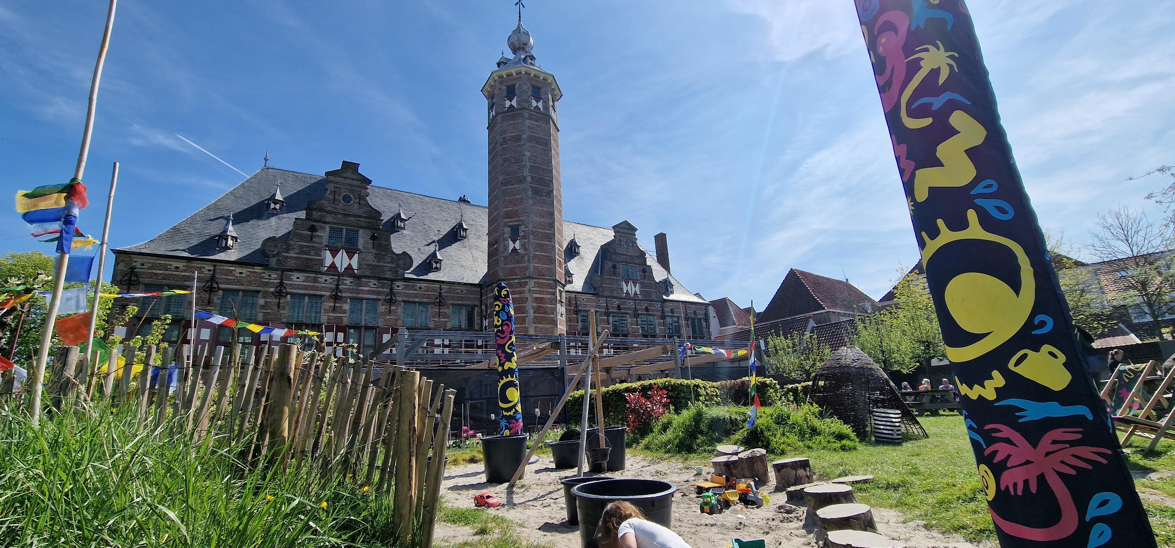Photo of the garden with the play area with sand and some water in the foreground and the monumental building in the background